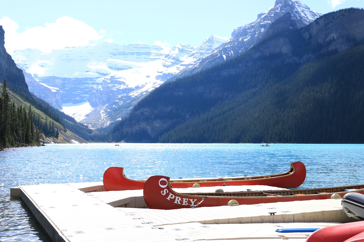 Canoe rosse ormeggiate a un pontile di legno su un lago di montagna, con le cime sullo sfondo