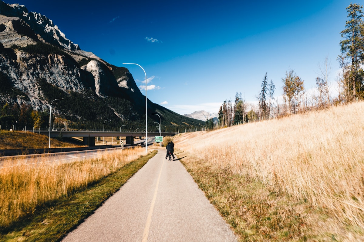 Un ciclista solitario su una pista ciclabile asfaltata tra i prati secchi, con le montagne sullo sfondo