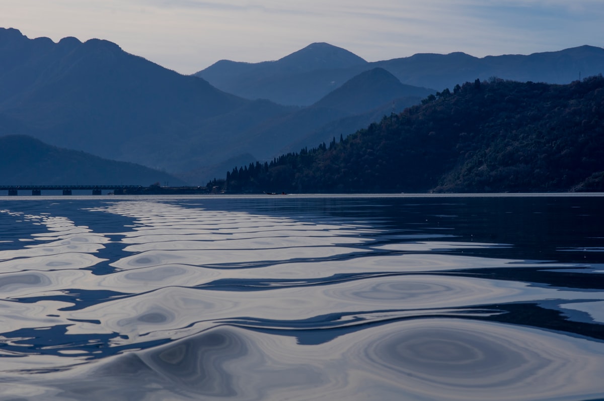 La superficie calma del lago con i riflessi dell'acqua e le montagne azzurre in lontananza